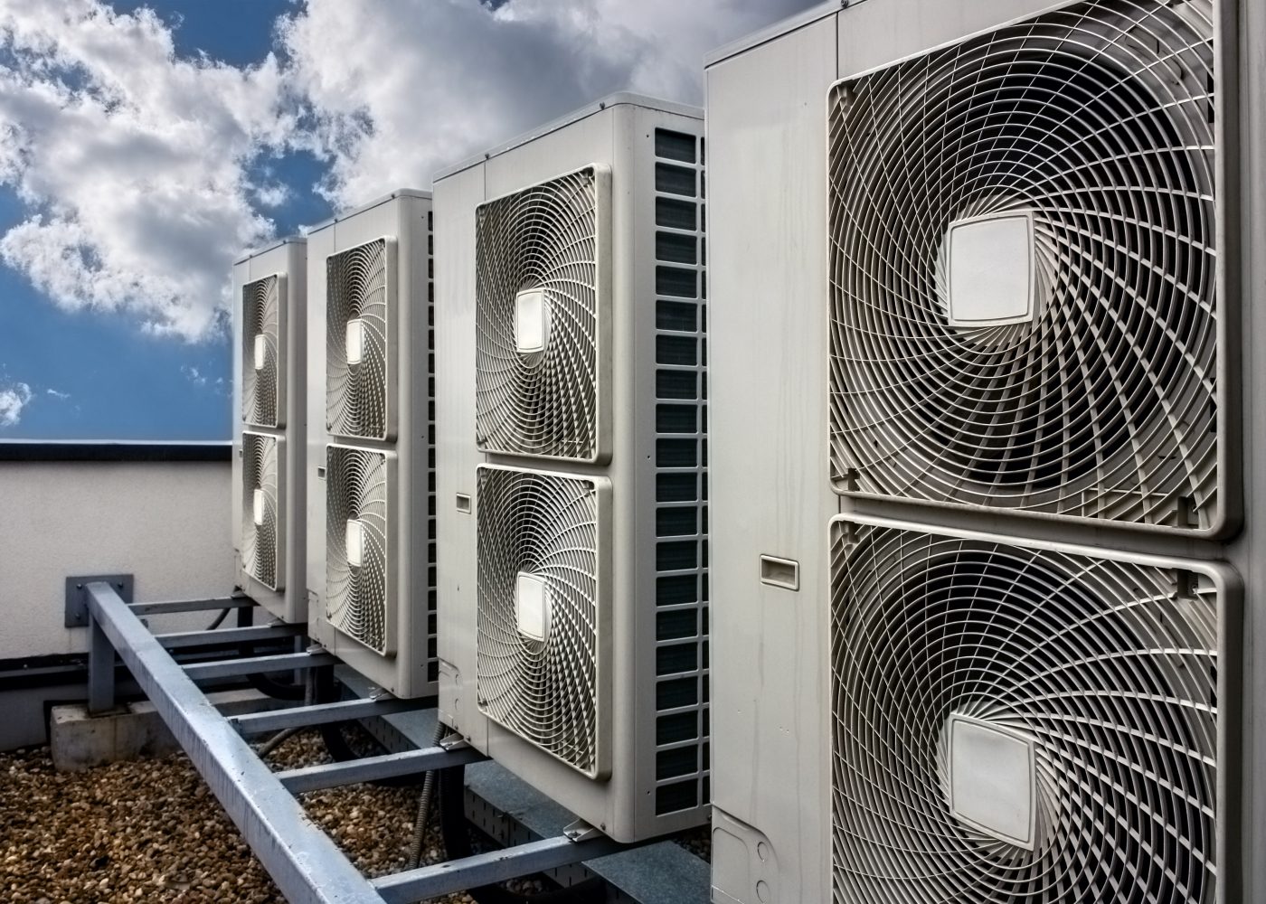 Rows of large air conditioning units on a rooftop, with cloudy sky in the background.