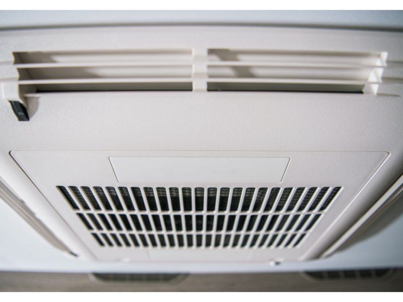 Close-up view of a ceiling-mounted air conditioning vent with slats and a central grille.