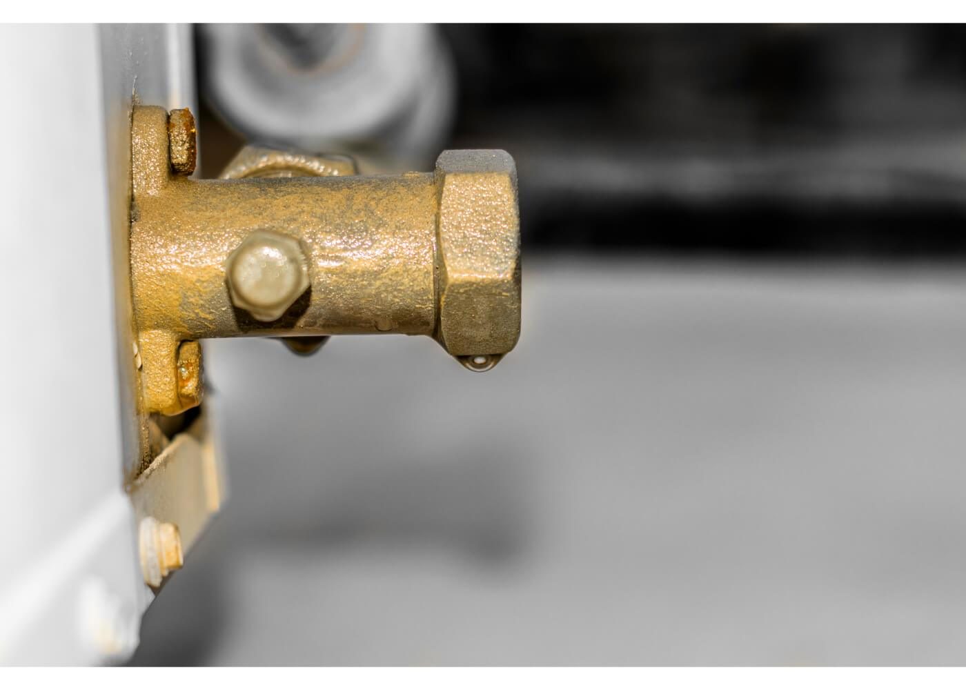 Close-up of a brass valve with a droplet of water forming at the edge, against a blurred background.