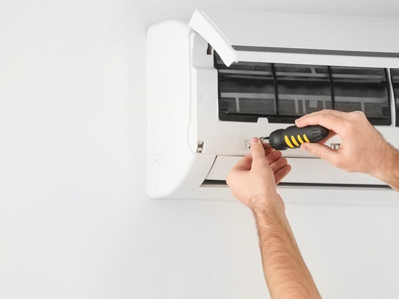 Person using a screwdriver to repair or install a wall-mounted air conditioning unit.