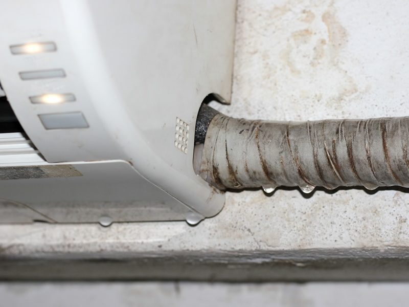 Close-up of an air conditioning unit dripping water, with condensation on a metal tube wrapped in insulation material.