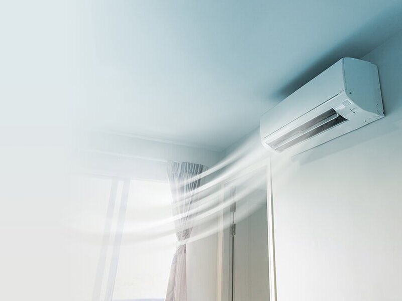 Wall-mounted air conditioner blowing cool air in a bright room with curtains.