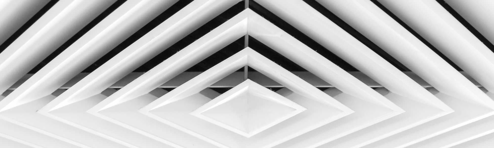 Close-up of a geometric ceiling vent with a symmetrical pattern of concentric diamond-shaped panels in white.