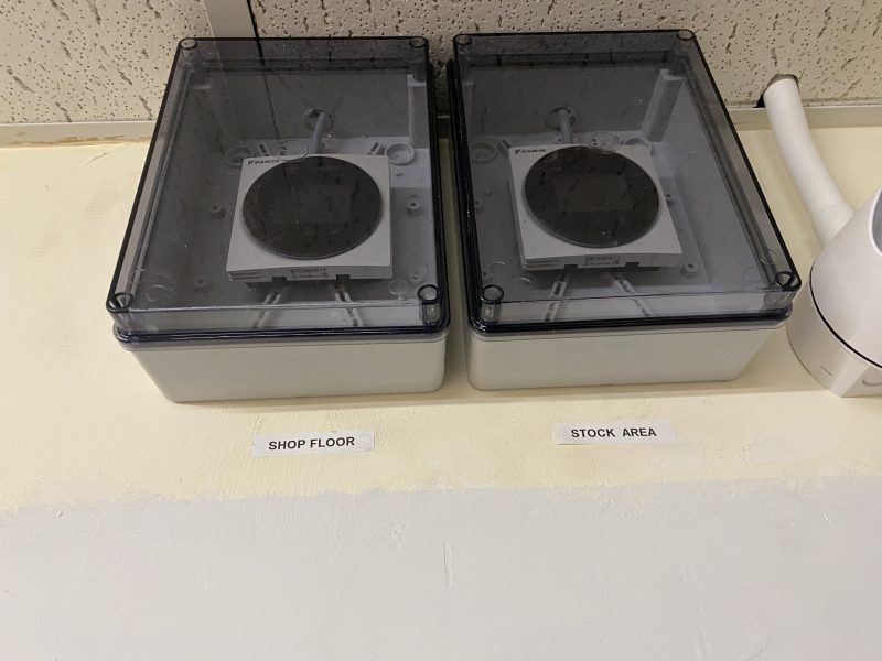 Two transparent electrical enclosures are mounted on a wall labeled "SHOP FLOOR" and "STOCK AREA.