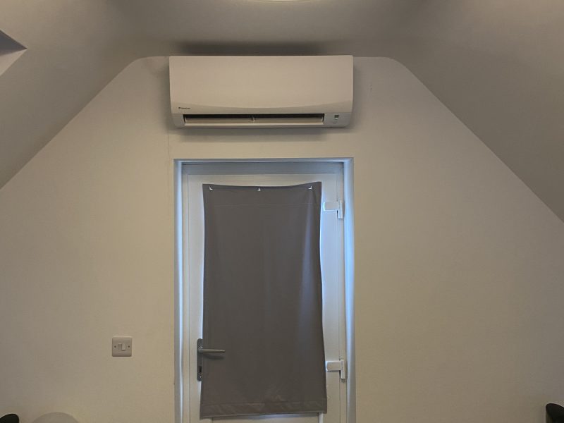 Room with a door covered by a gray cloth, an air conditioning unit above, a round ceiling light, and a dark speaker on each side.