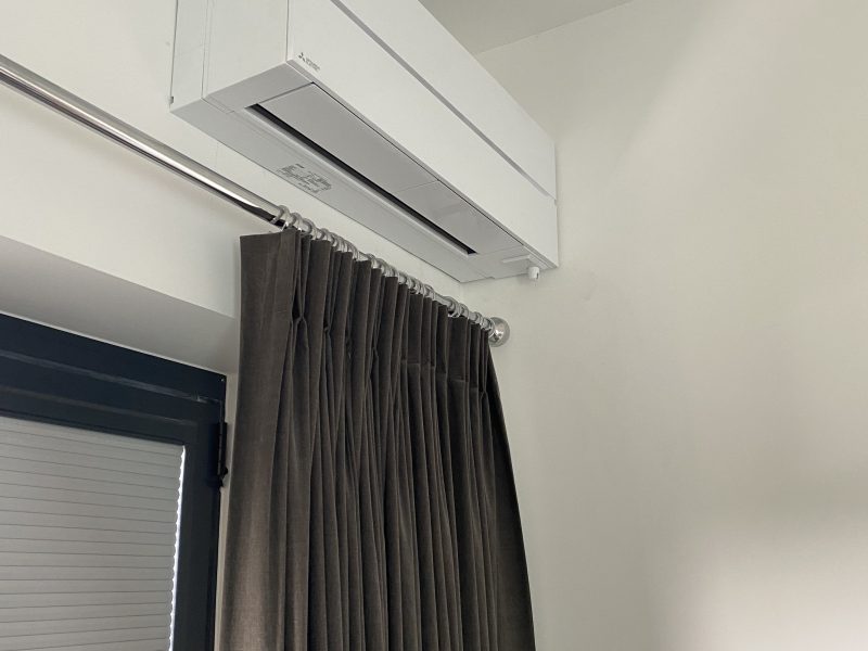 Wall-mounted air conditioning unit above a closed window with dark curtains.