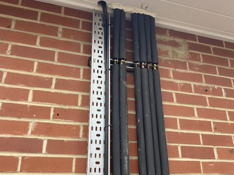 Four black insulated pipes run vertically along a brick wall, secured with clips.