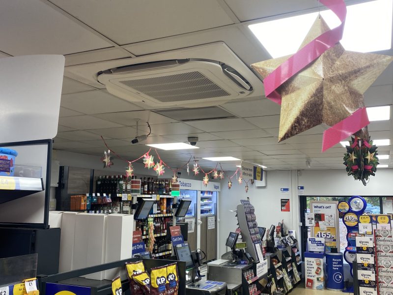 A convenience store interior with holiday decorations, snacks on display, and a checkout area. Ceiling features a star ornament and festive garland.