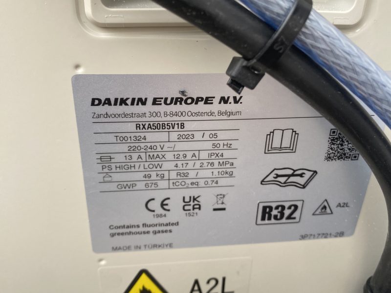 Close-up of a Daikin Europe air conditioning unit label, showing model RXA50B5V1B, specifications, and safety symbols, including refrigerant type R32 and a flammable gas warning.