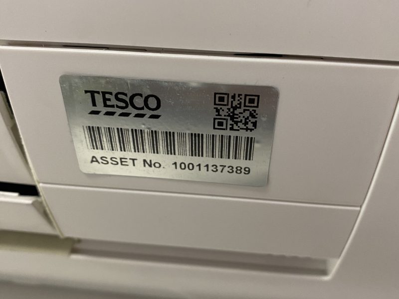 Close-up of a white surface with a silver label reading "TESCO" and "ASSET No. 1001137389," featuring a barcode and QR code.